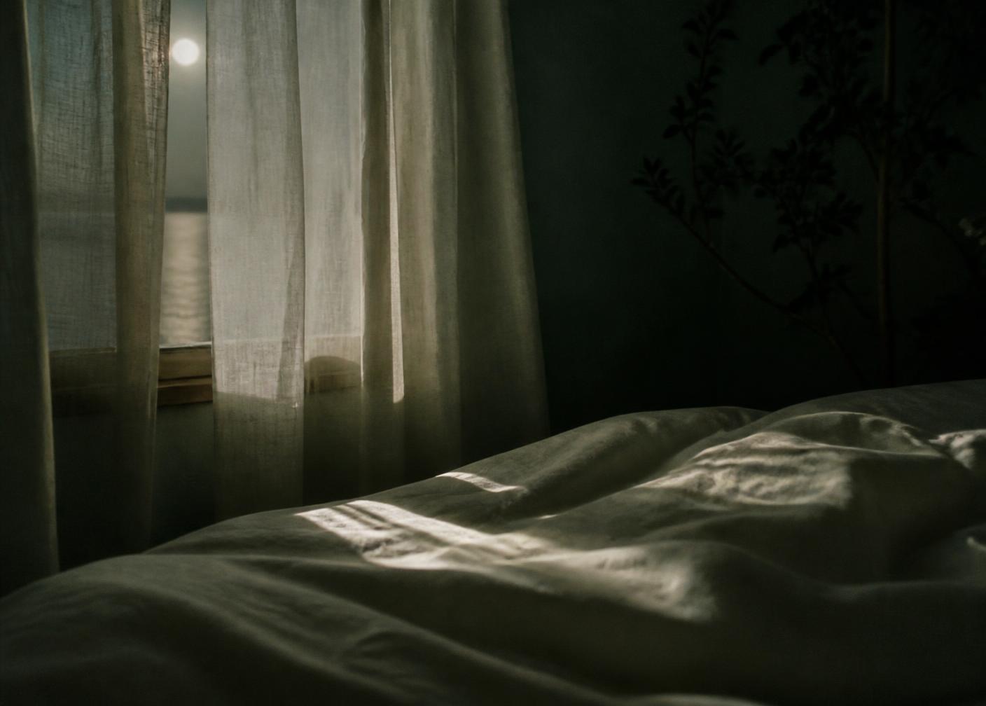 Moonlight falling through sheer linen curtains onto quiet bedsheets